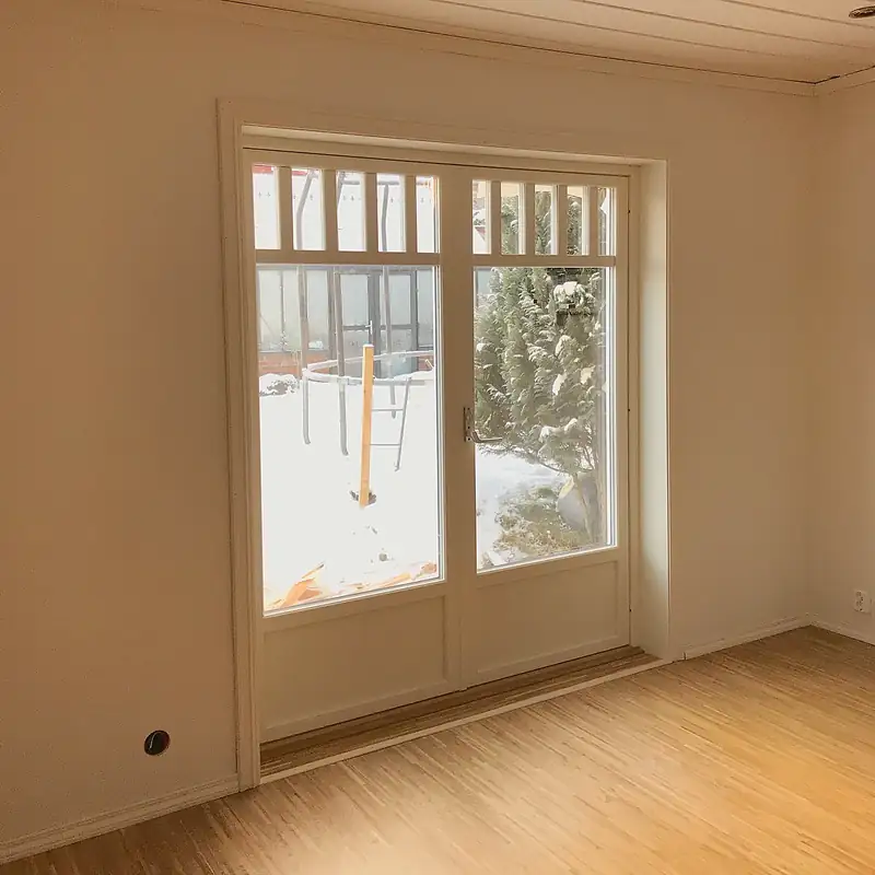 Hvit tofløyet dør med store glassfelt og en rad smale ruter øverst, i et tomt rom med lyst tregulv. Utenfor ligger det snø i hagen.