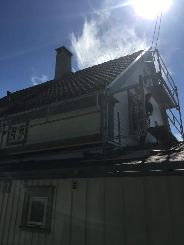 Motlysbilde av huset nedenfra. Et stillas står over den lave delen av huset, opp mot gavlen, og en person står på stillaset.